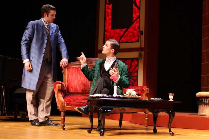 a man in a coat and a man in a suit sitting on a stage