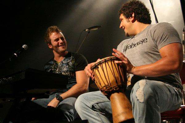 a man sitting next to another man playing a drum