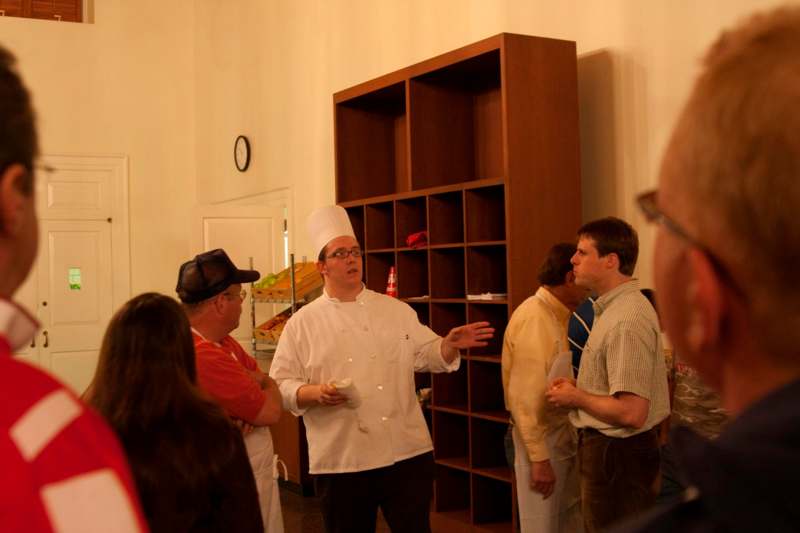 a man in a chef's hat and white coat standing in a room with a group of people