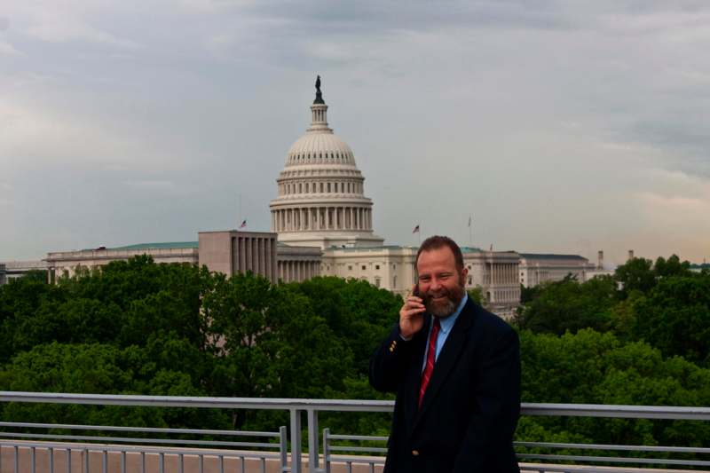 a man in a suit talking on a cell phone in front of a capitol building with United States Capitol in the background