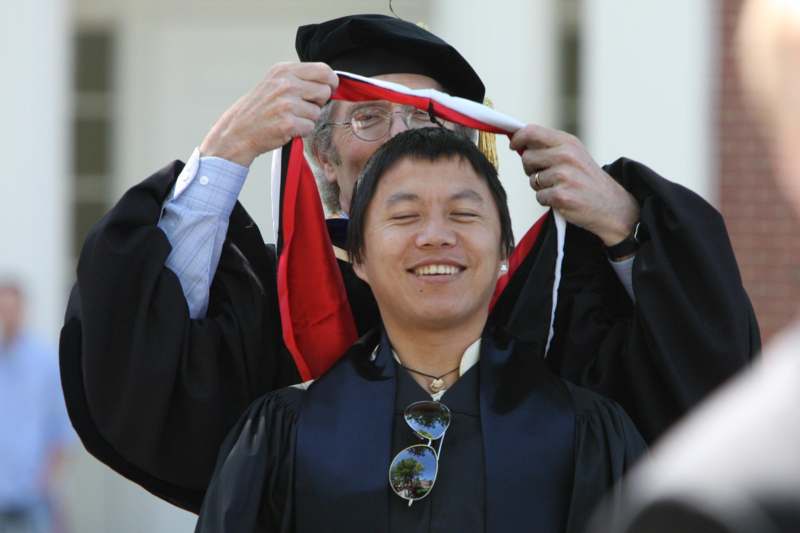 a man in a graduation gown holding a red scarf over his head