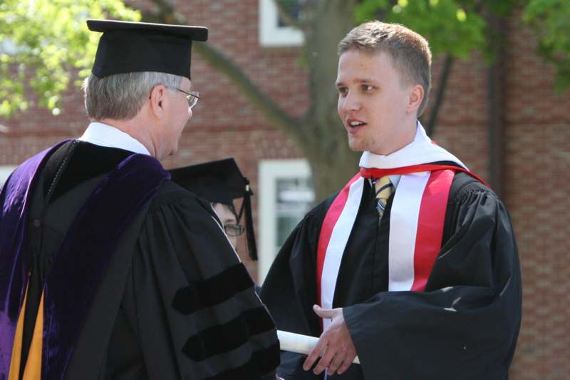 a man in a graduation gown talking to a man in a cap and gown