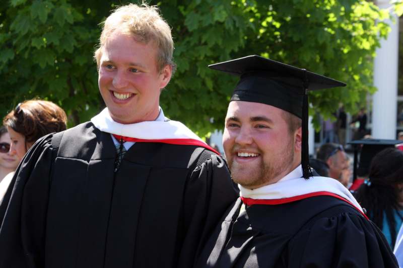 a man in black gown and cap standing next to another man in black gown and cap