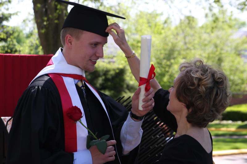 a man in a graduation gown and cap putting on a diploma