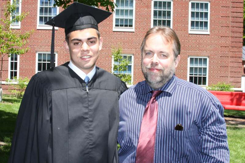 a man in a graduation gown and cap standing next to a man in a striped shirt