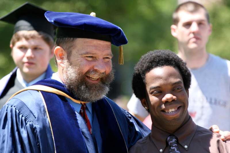 a man in a graduation gown and cap smiling