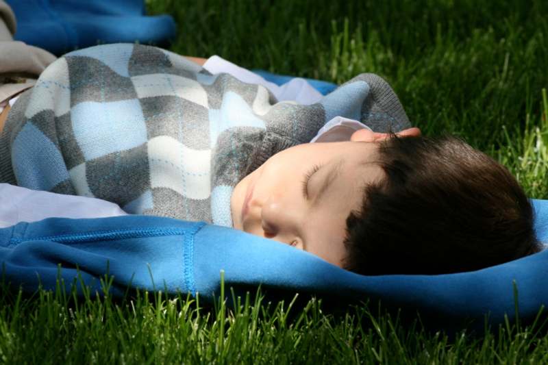 a boy sleeping on a blanket in the grass