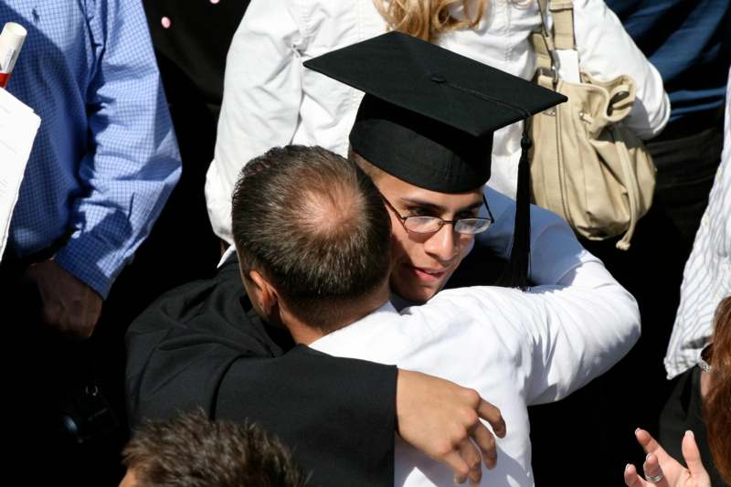 a man in a graduation cap and gown hugging a man