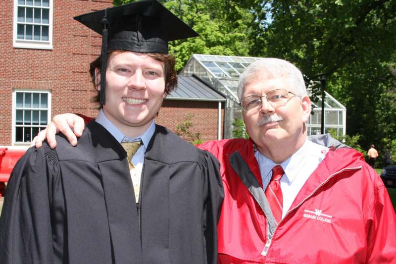 a man in a graduation gown and cap standing next to a man in a red robe