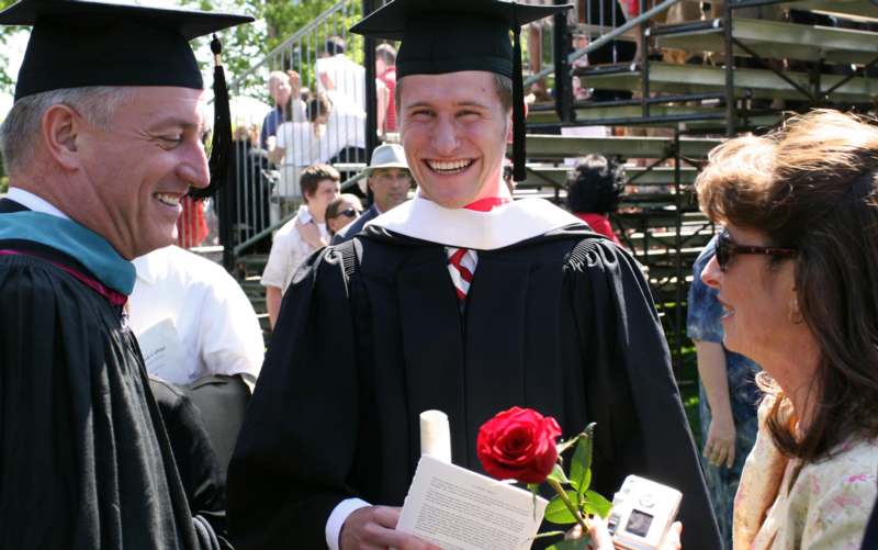a man in graduation gown holding a rose