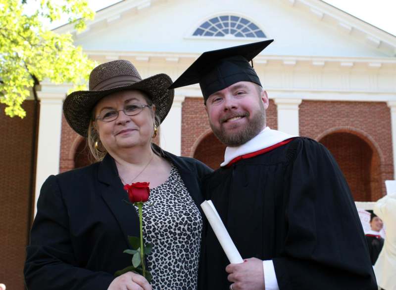 a man and woman in graduation gowns and hat holding a rose
