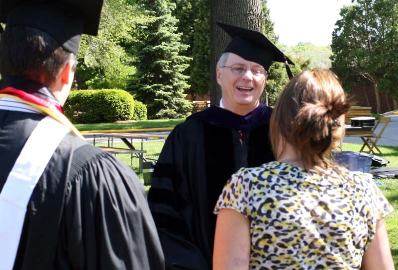 a man in a cap and gown talking to a group of people