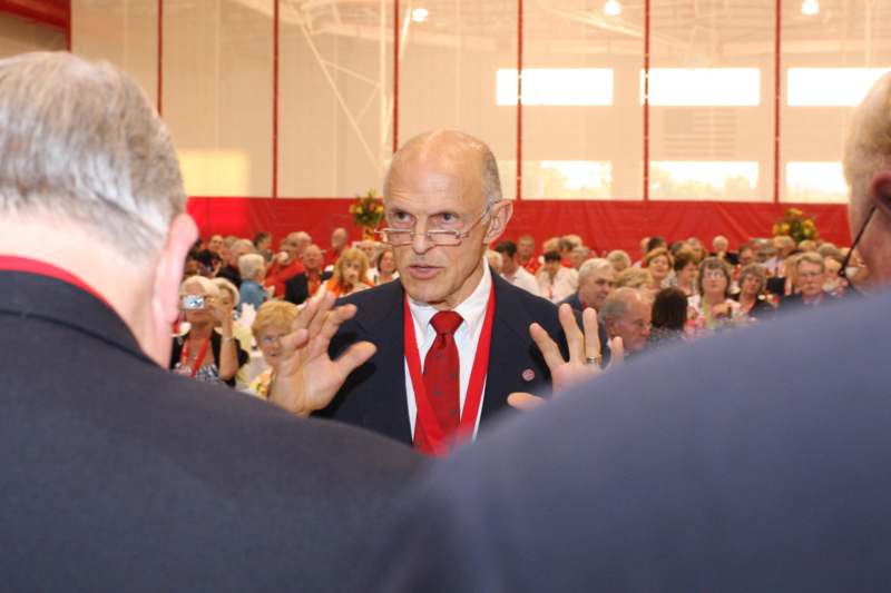 a man in a suit and tie talking to a crowd of people