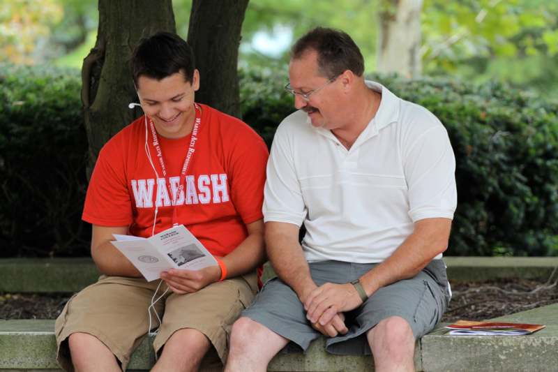 a man and a man sitting on a bench looking at a book