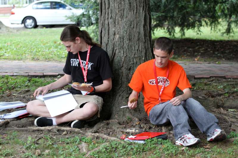 a couple of young men sitting under a tree eating food