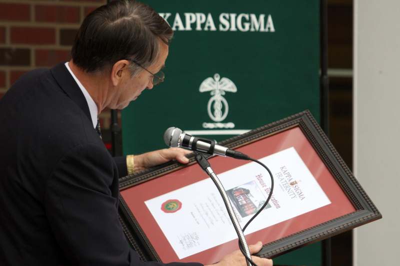 a man holding a microphone and a framed certificate