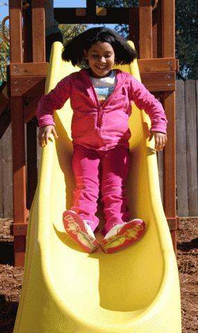 a girl in a pink jacket and pink pants on a yellow slide