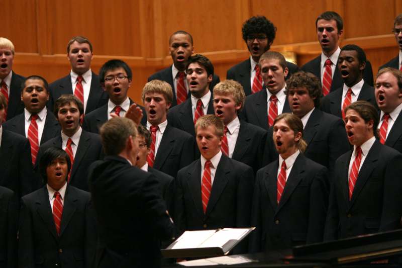 a group of men wearing suits and red ties singing