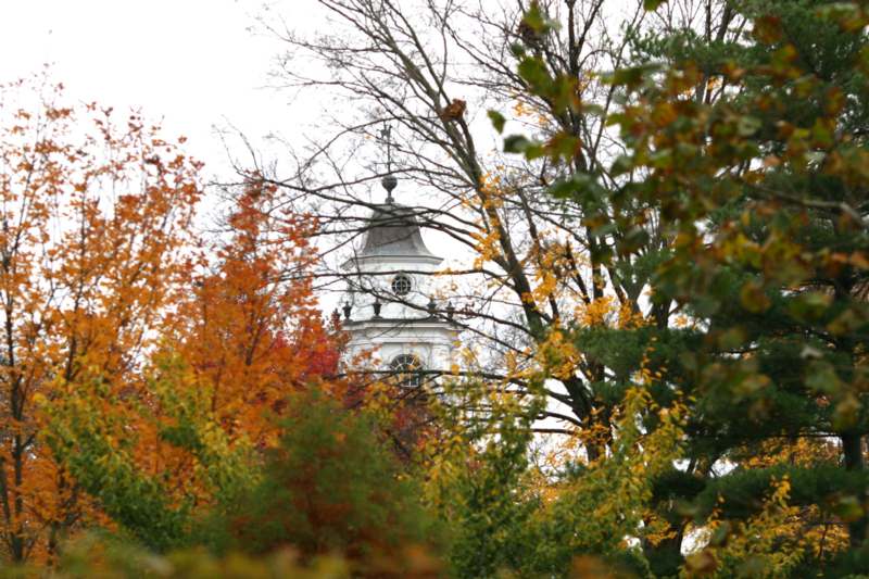 a white building with a cross on top and trees with fall leaves