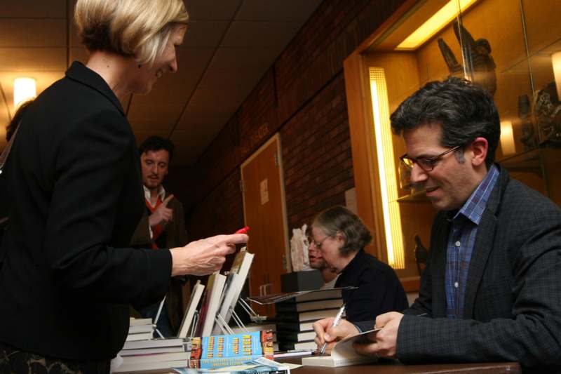 a woman looking at a man signing a book