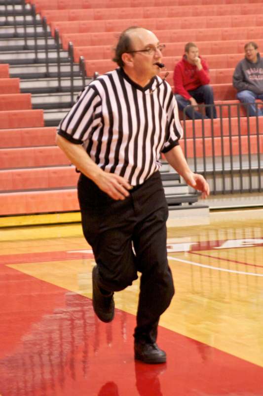 a man wearing a referee shirt and a helmet running on a basketball court