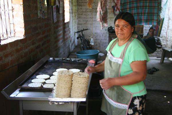 a woman making tortillas in a kitchen