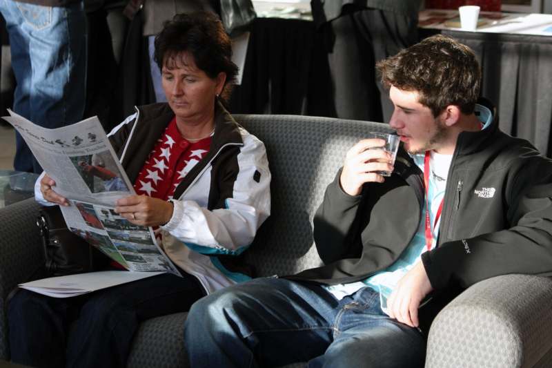 a man and woman sitting on a couch reading a newspaper