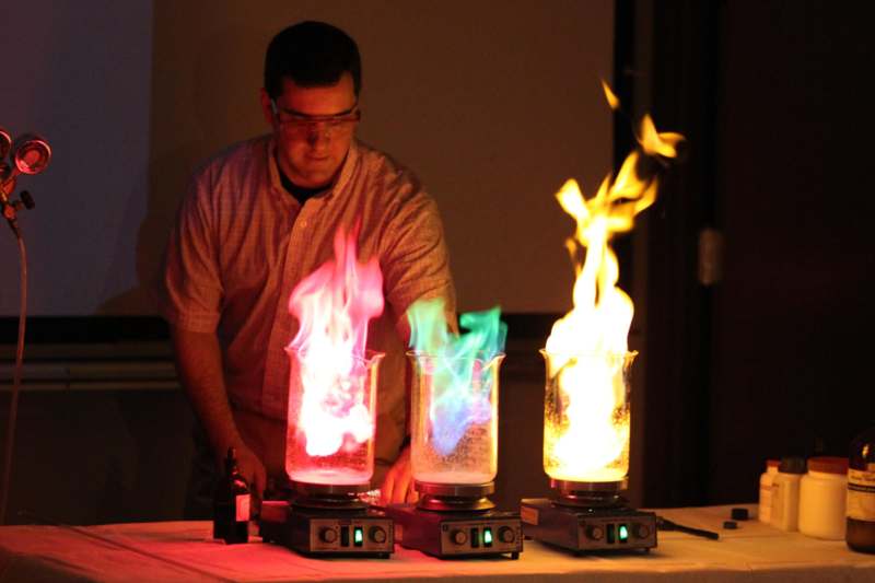 a man standing next to several glass containers with colorful flames
