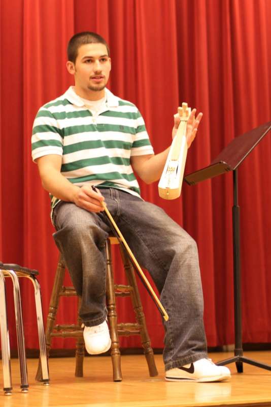 a man sitting on a stool holding a stringed instrument