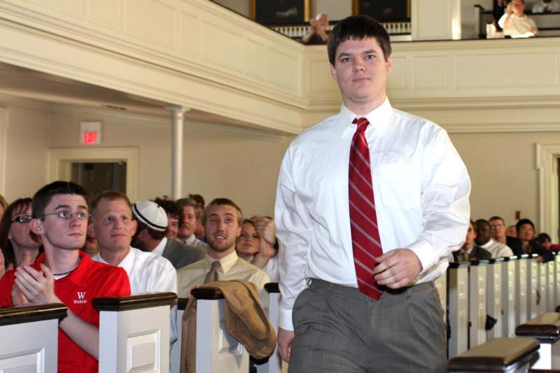 a man in a white shirt and red tie walking in a room with people