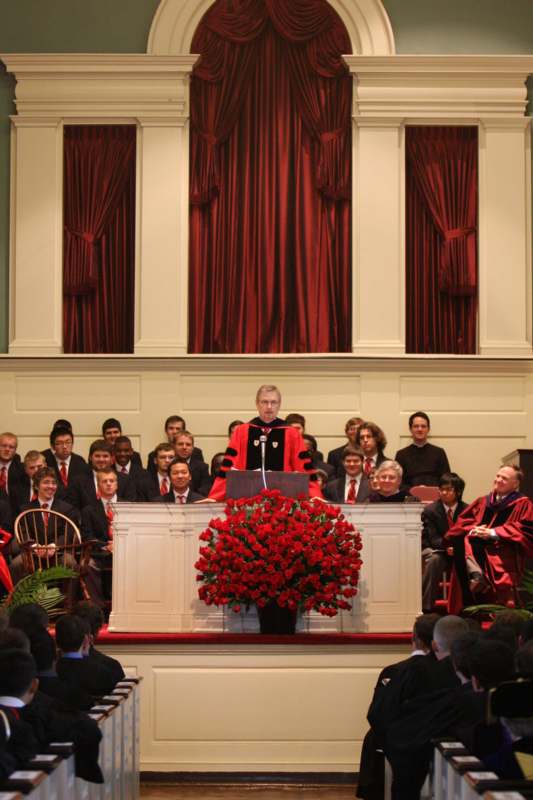 a man in a red robe standing at a podium with a group of people in the background