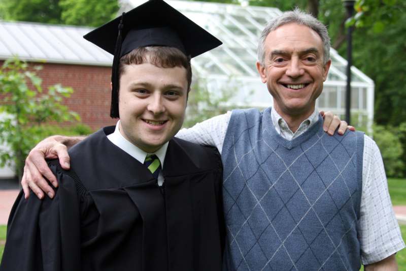 a man in a graduation gown and cap standing next to a man in a vest