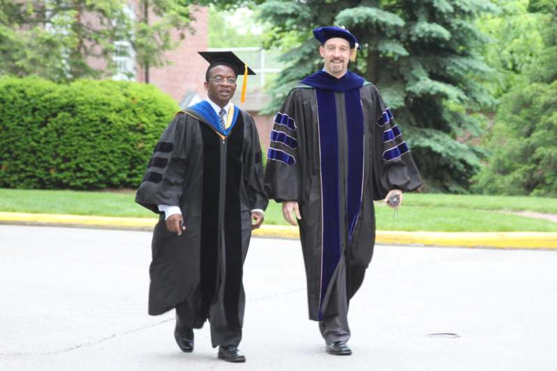 a man in graduation gowns walking down a street
