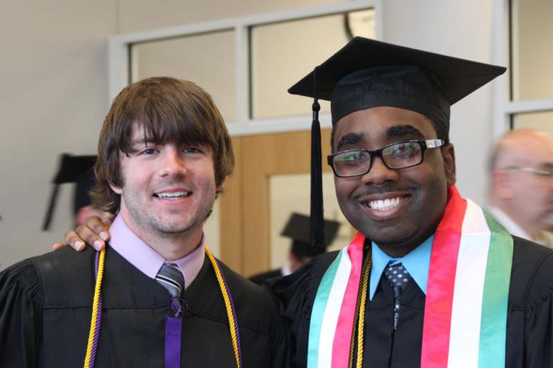 a man in graduation gown and cap with his arm around another man