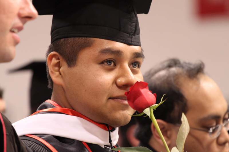 a man in a graduation cap and gown holding a rose