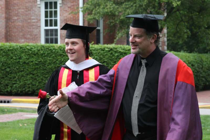 a man in graduation gowns and cap shaking hands with a man in a cap and gown