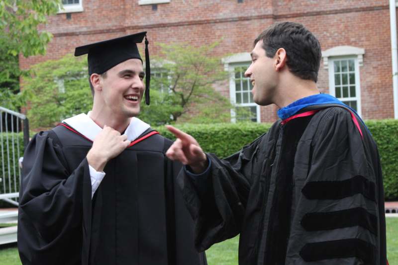 a man in graduation gowns pointing at another man