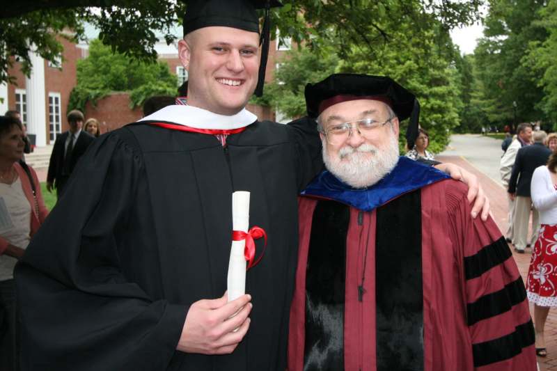 a man in a graduation gown and cap standing next to a man in a cap and gown