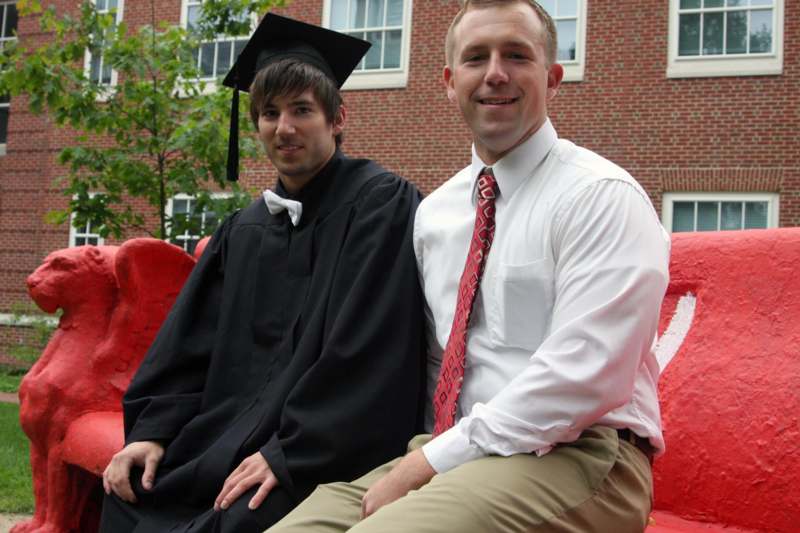 a man in a graduation gown and cap sitting next to another man