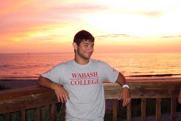 a man leaning on a railing with a sunset behind him