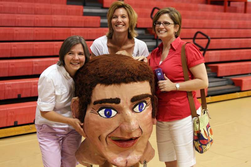 a group of women posing with a large man's head