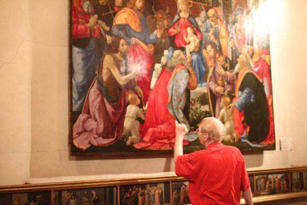 a man in a red shirt pointing at a painting
