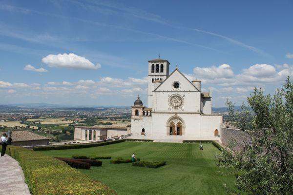 a white building with a large lawn with Assisi in the background