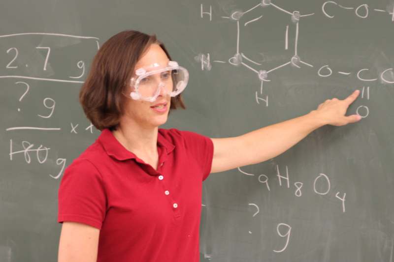 a woman wearing goggles and pointing at a chalkboard
