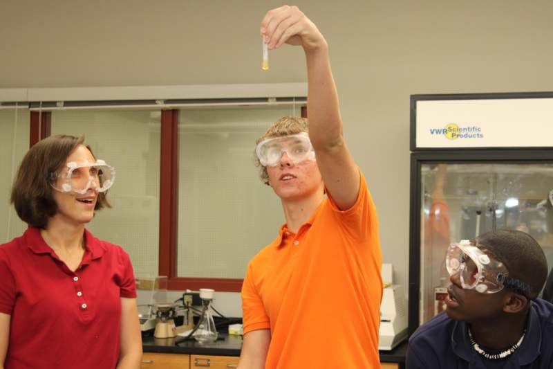 a group of people in safety goggles holding a tube with liquid