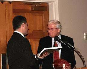 a man in a suit holding a book and speaking to another man