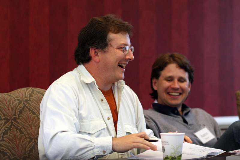 a man laughing while another man sits at a table