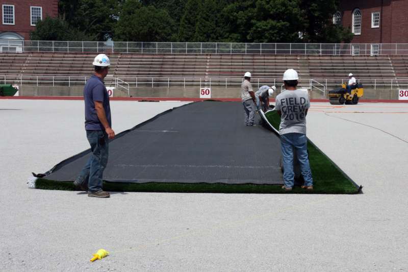 men in hardhats laying a turf on a stadium