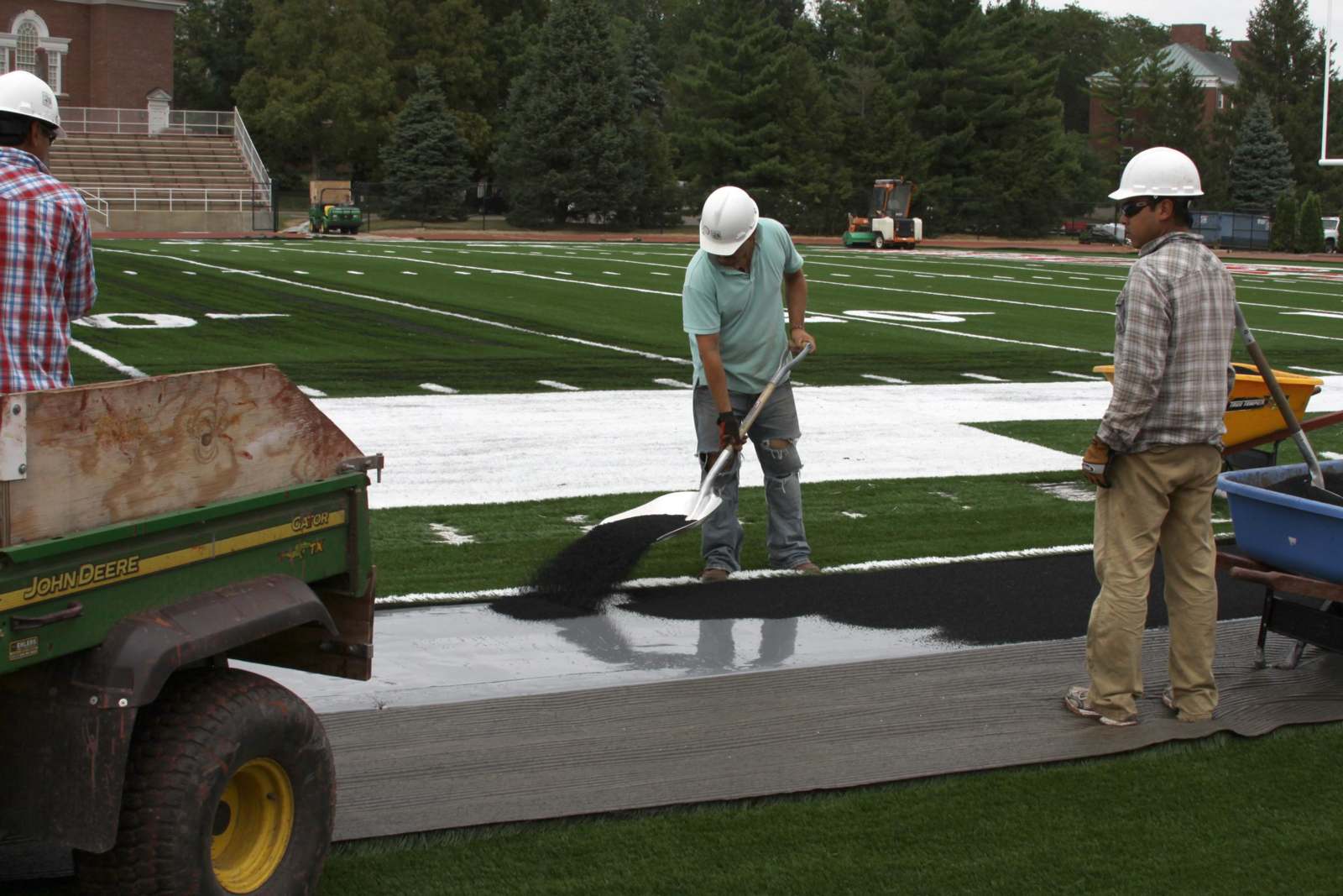 men wearing hardhats using a shovel to clean a football field
