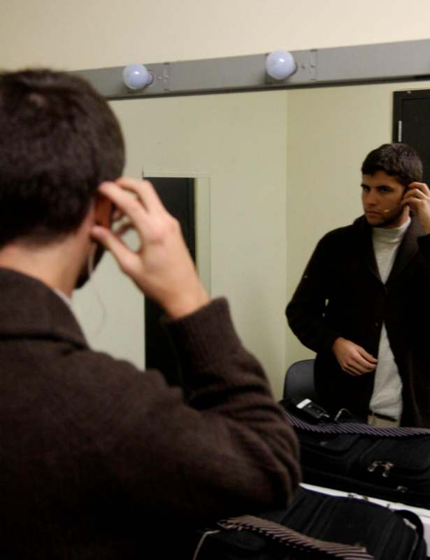 a man in a brown jacket talking on a phone in front of a mirror
